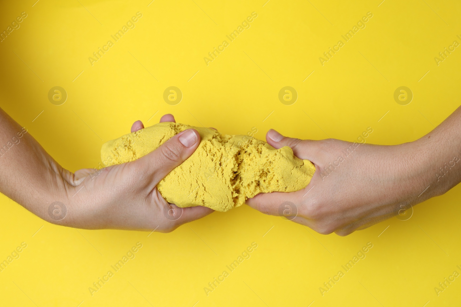 Photo of Woman playing with kinetic sand on yellow background, top view