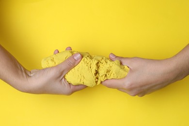 Woman playing with kinetic sand on yellow background, top view