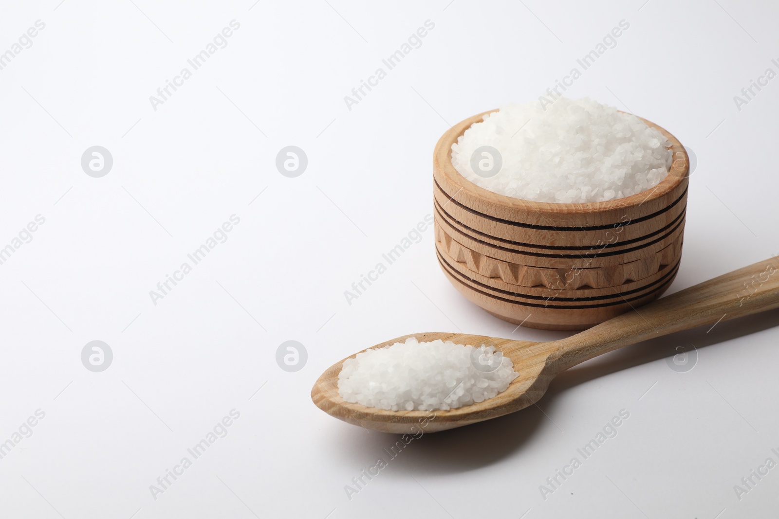 Photo of Natural salt in wooden spoon and bowl on white background, space for text