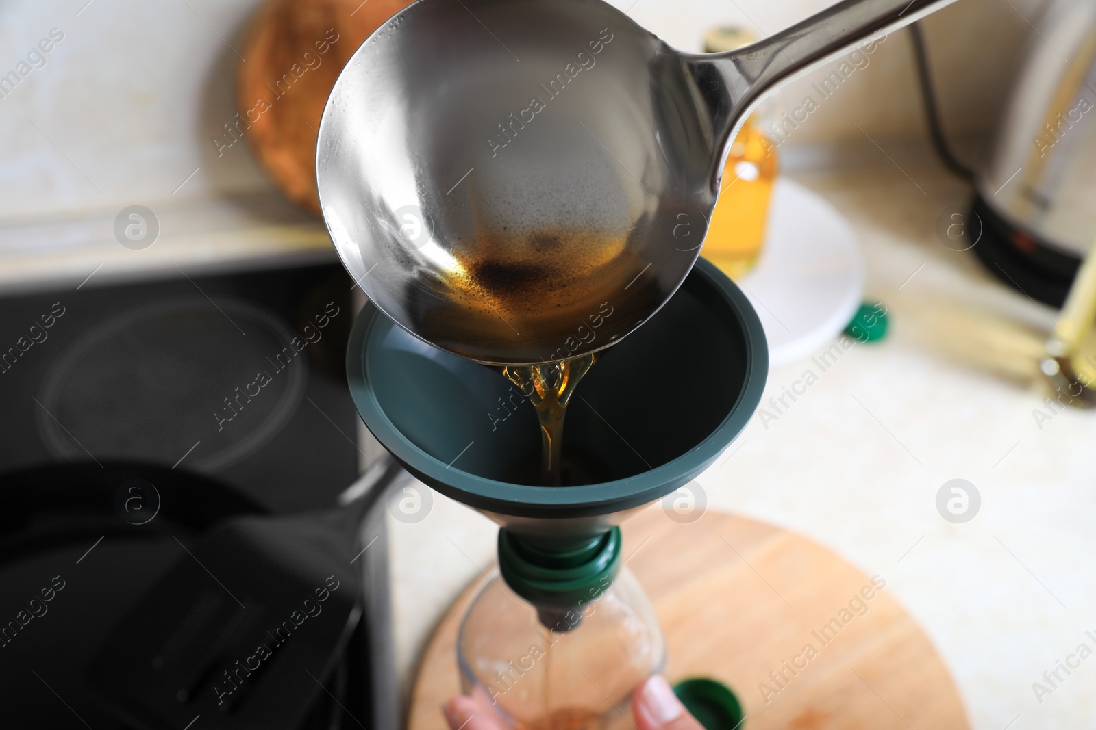 Photo of Woman pouring used cooking oil into bottle through funnel in kitchen, closeup