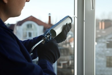 Construction worker sealing window with caulk indoors, closeup