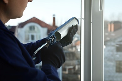 Photo of Construction worker sealing window with caulk indoors, closeup