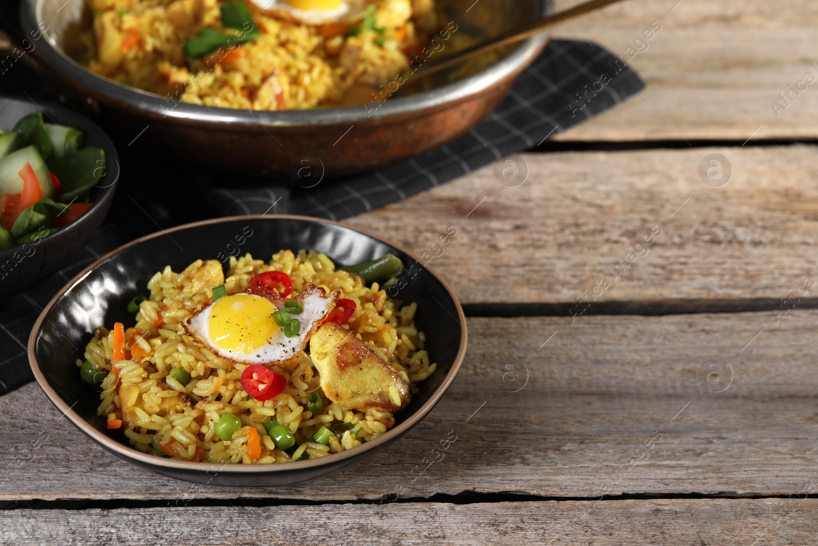 Photo of Tasty rice with meat, egg and vegetables in bowl served on wooden table. Space for text