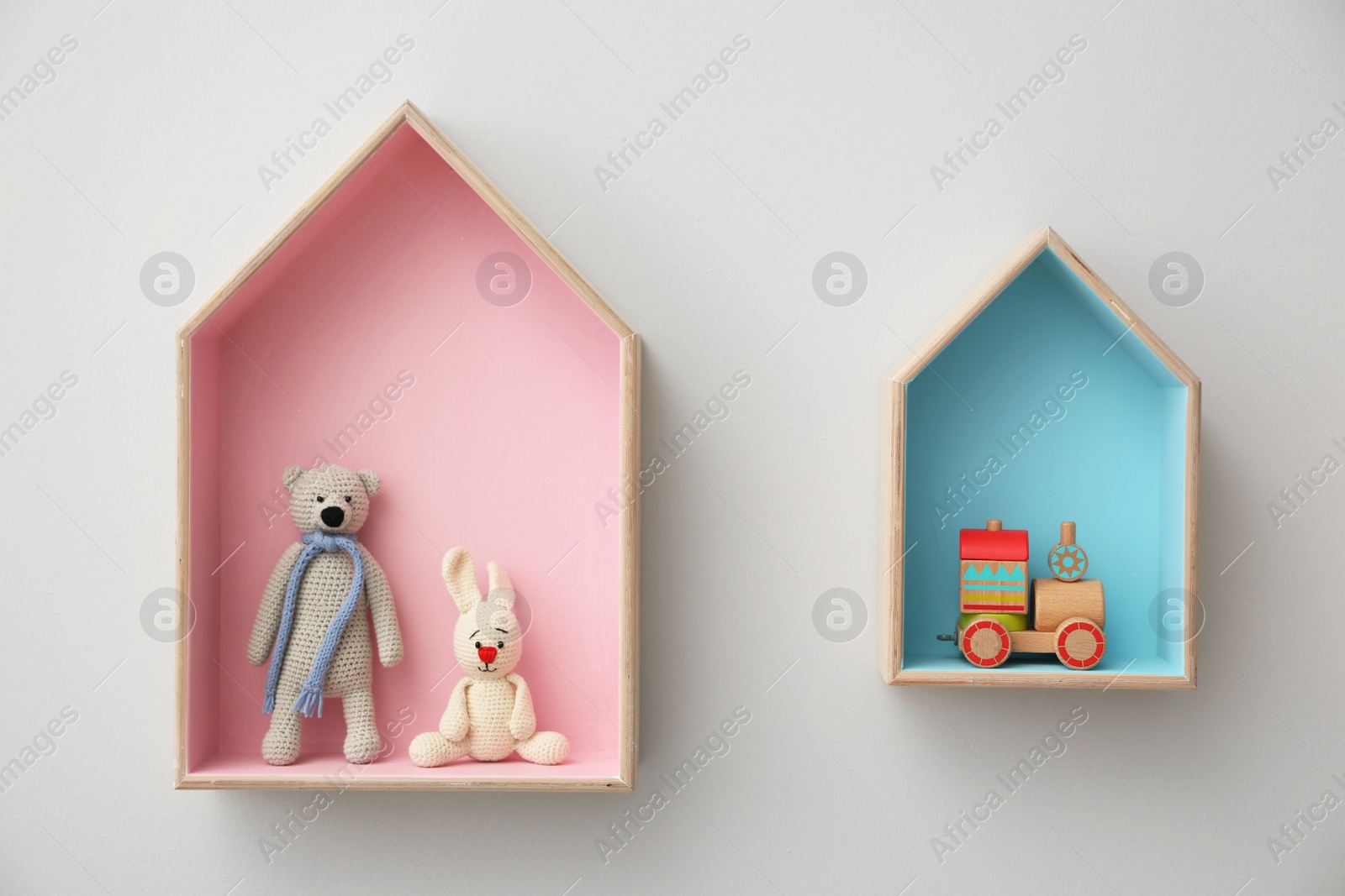 Photo of Stylish house shaped shelves with toys on white wall. Baby room interior design