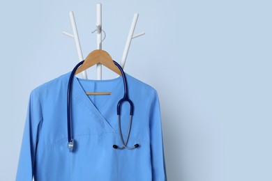 Photo of Medical uniform and stethoscope hanging on rack against light grey background. Space for text