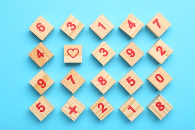Photo of Wooden cubes with numbers and different symbols on light blue background, flat lay