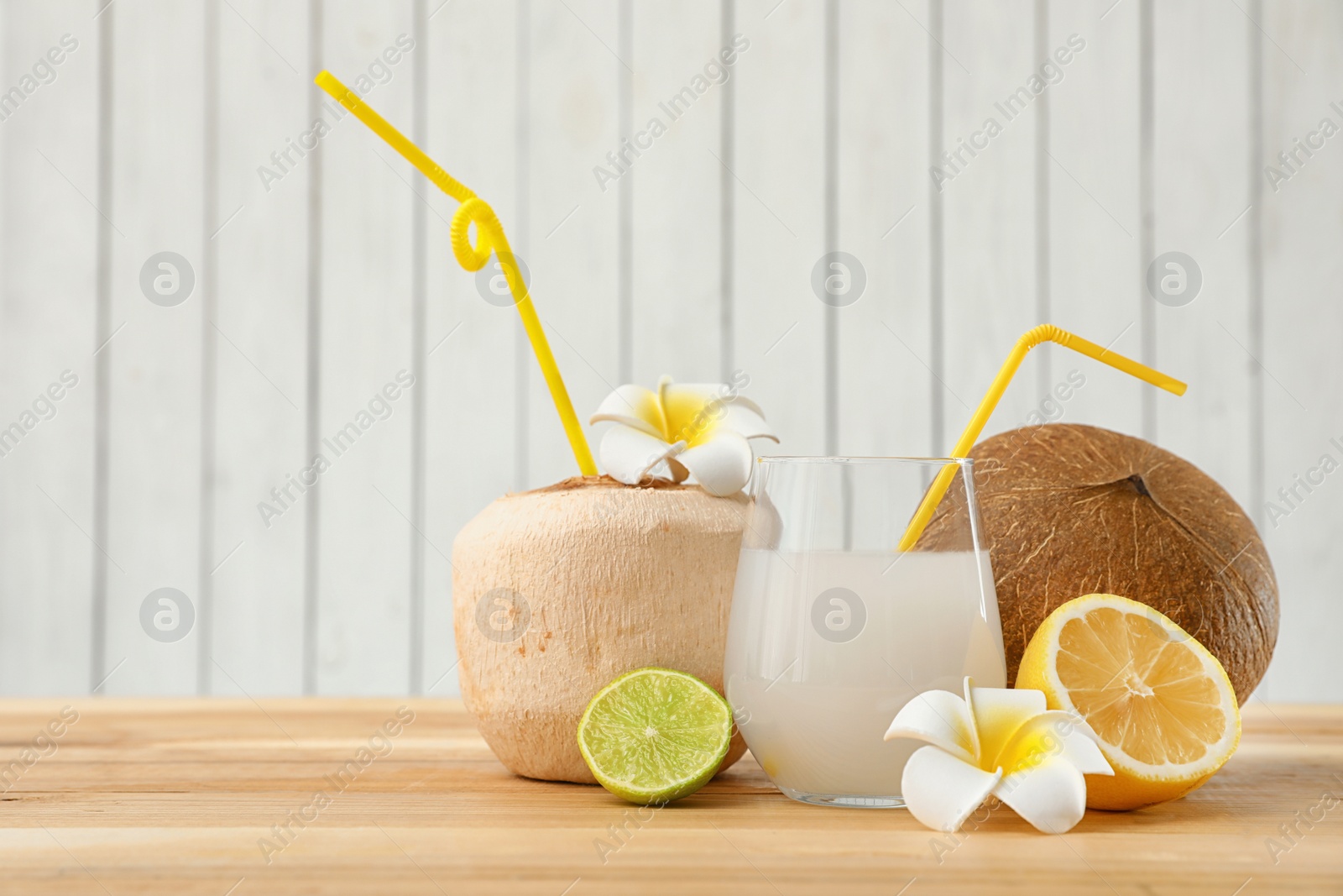 Photo of Composition with glass of coconut water on wooden table against light background