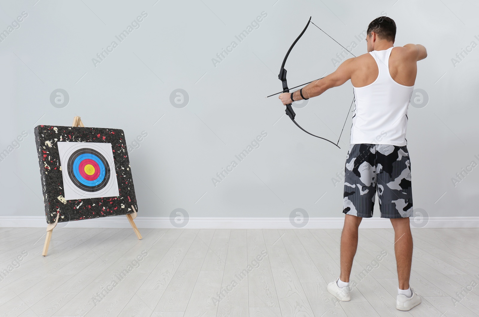 Photo of Man with bow and arrow aiming at archery target indoors