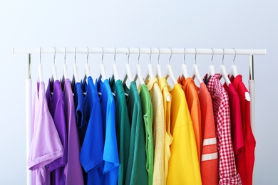 Rack with rainbow clothes on light background