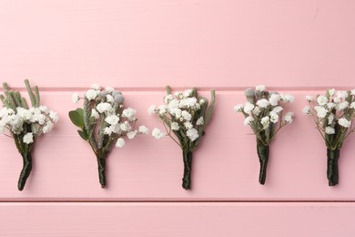 Many small stylish boutonnieres on pink wooden table, flat lay
