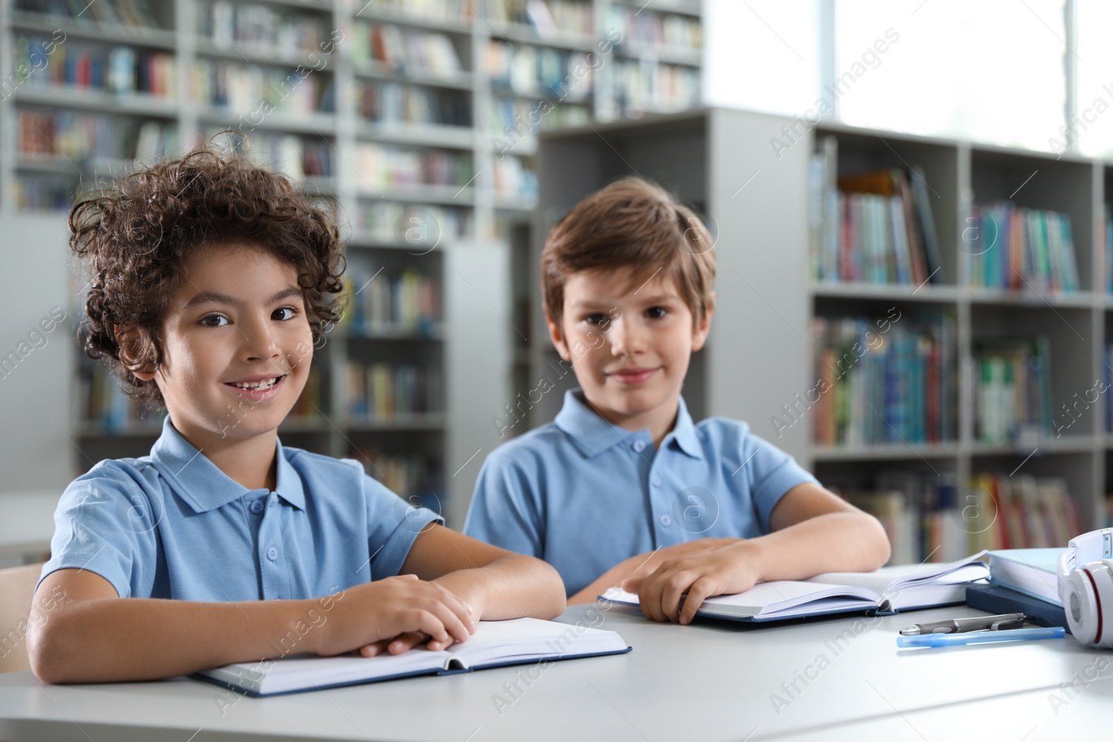 Photo of Cute little boys reading books at table in library