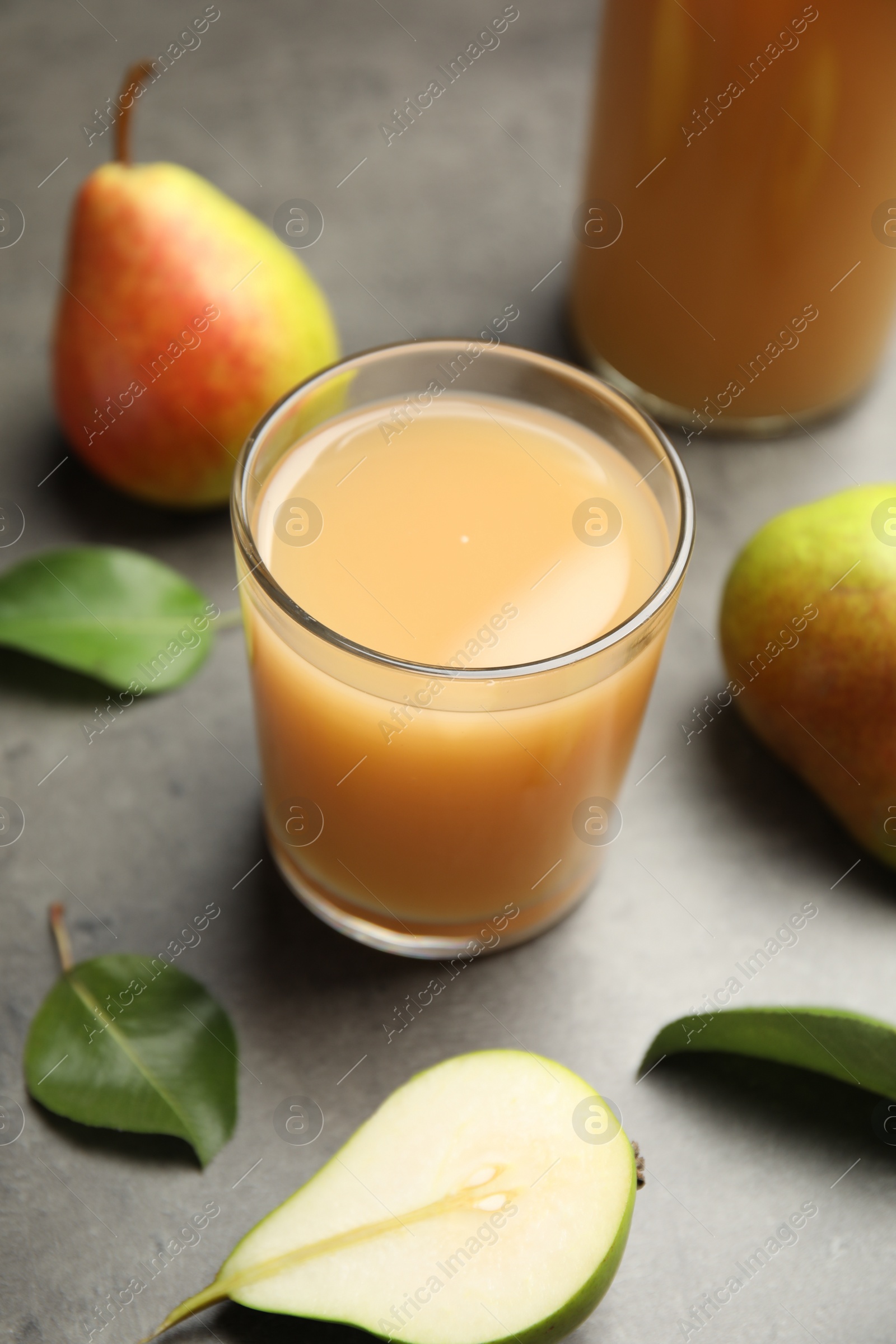 Photo of Tasty pear juice, fruits and leaves on grey table