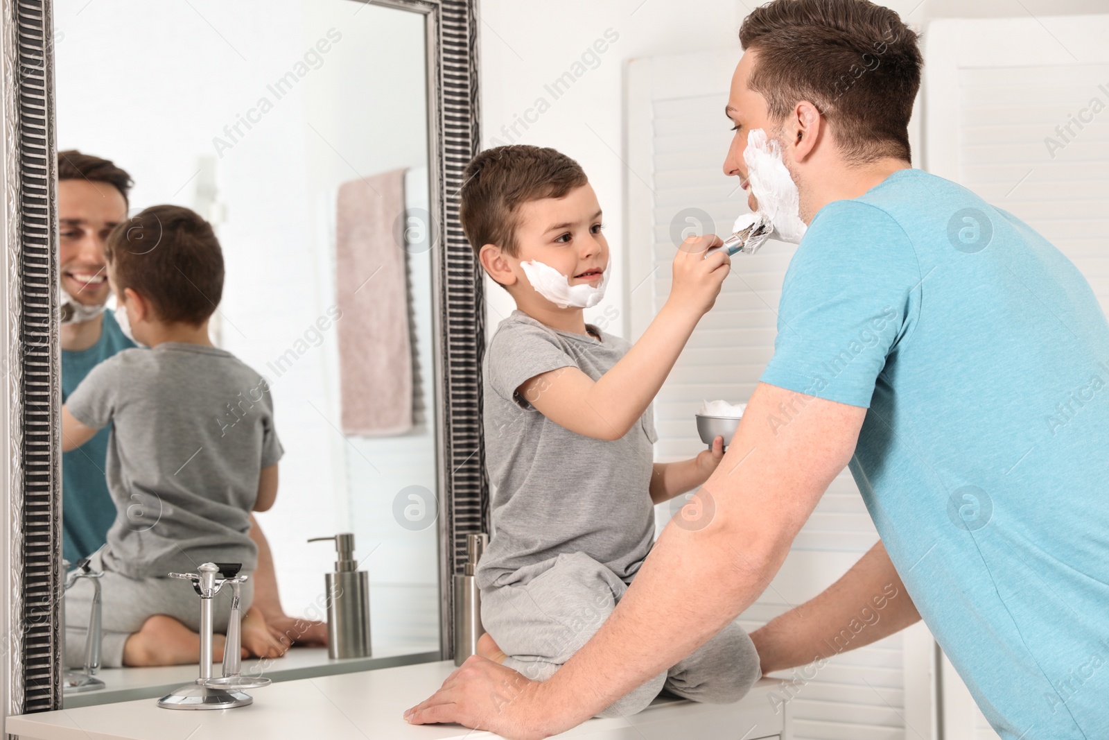 Photo of Little son applying shaving foam onto dad's face in bathroom