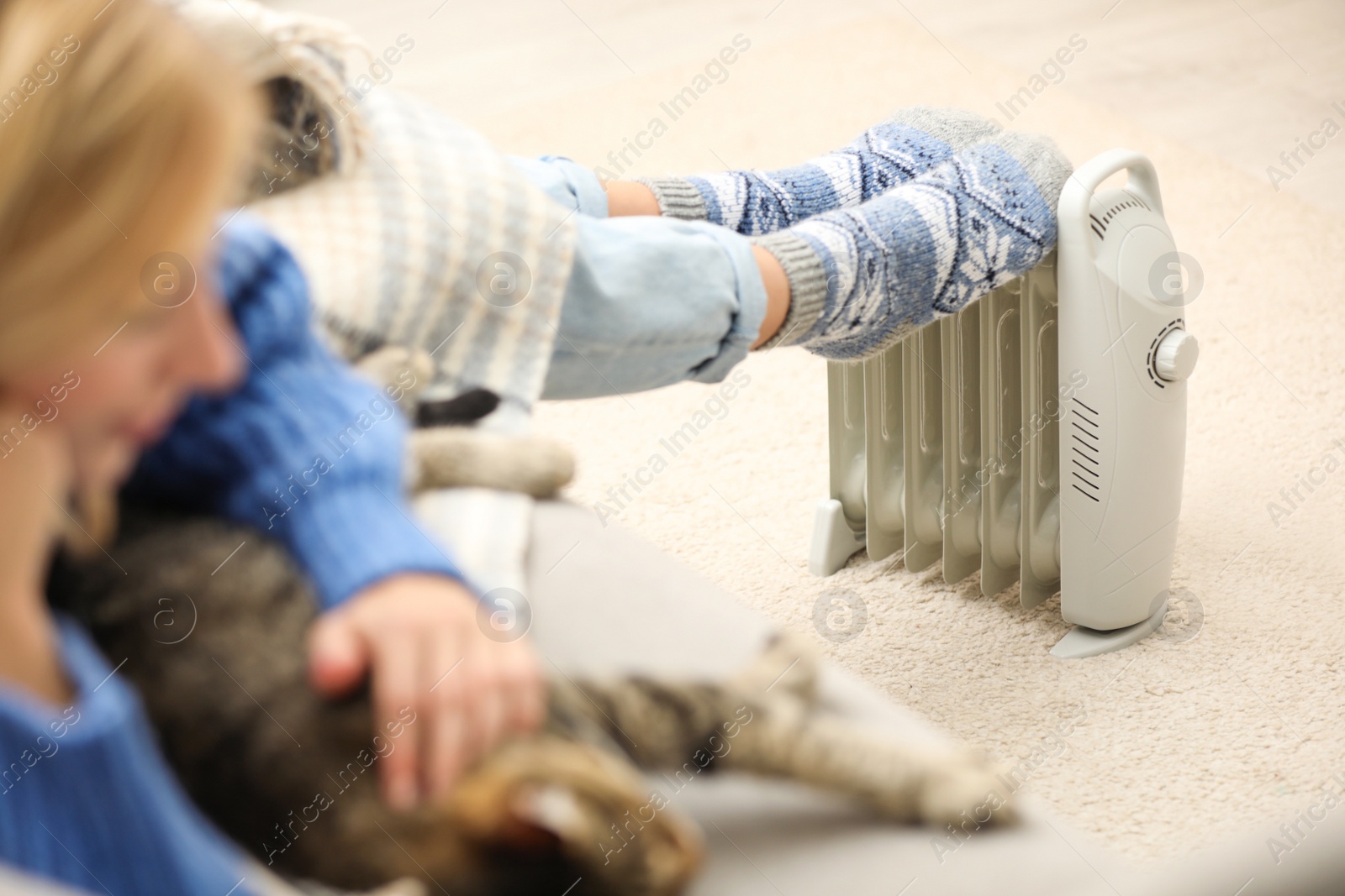 Photo of Woman warming feet on electric heater at home, closeup