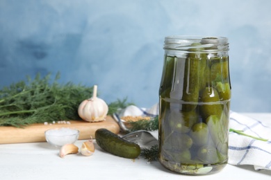Photo of Jar with pickled cucumbers on white wooden table against blue background