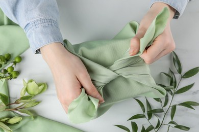 Photo of Furoshiki technique. Woman wrapping gift in green fabric at white table, top view