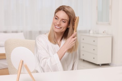 Photo of Beautiful woman brushing her hair at vanity in bedroom