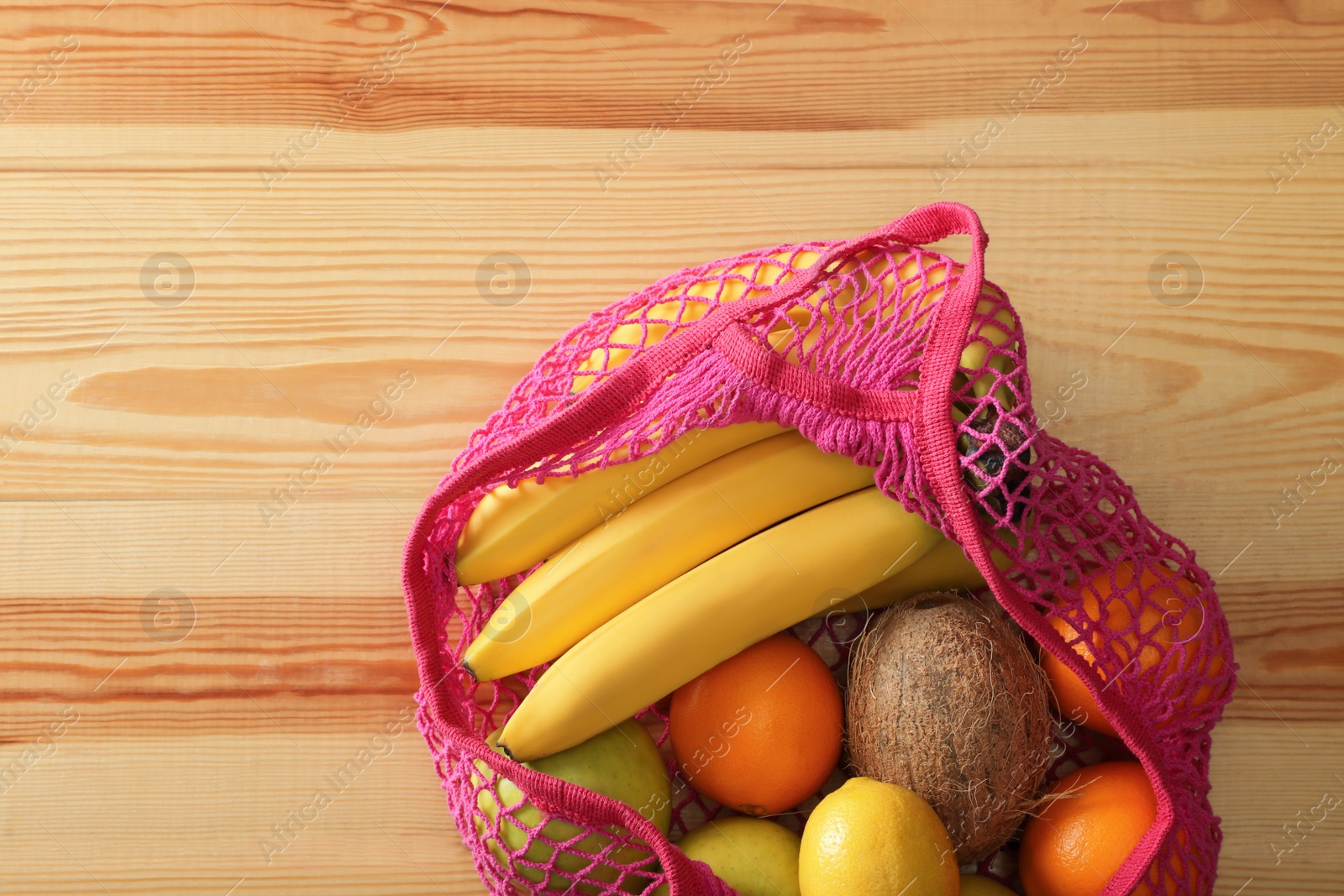 Photo of Net bag with fruits on wooden table, top view. Space for text