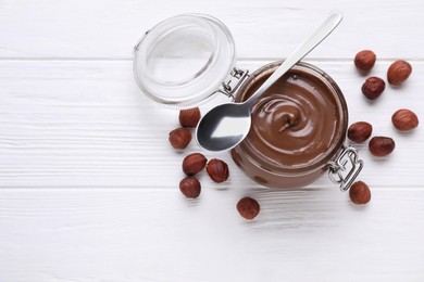 Jar with delicious chocolate paste and nuts on white wooden table, flat lay. Space for text