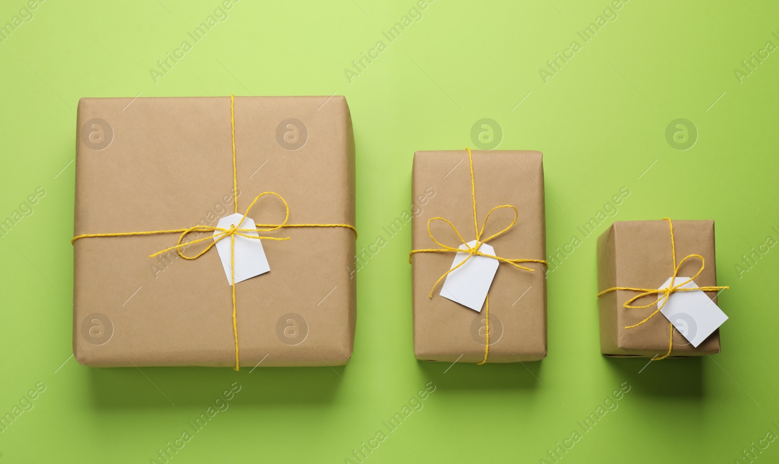 Photo of Parcels wrapped in kraft paper with tags on green background, flat lay