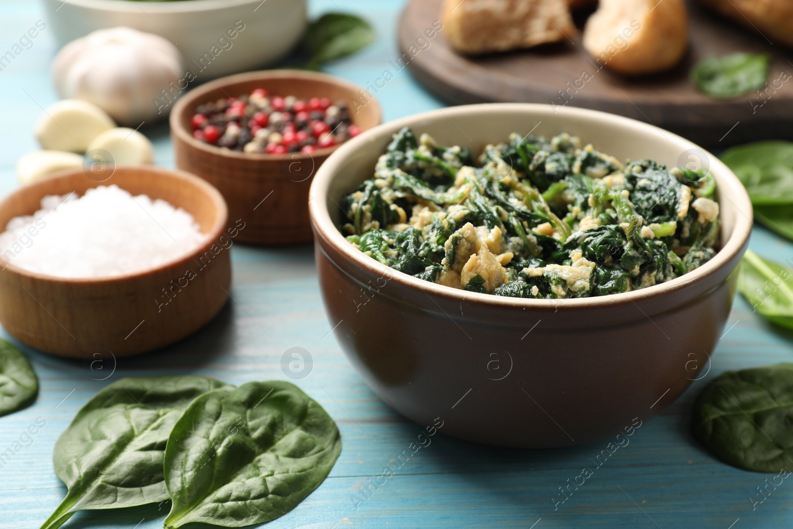 Photo of Tasty spinach dip with egg in bowl and spices on light blue wooden table, closeup