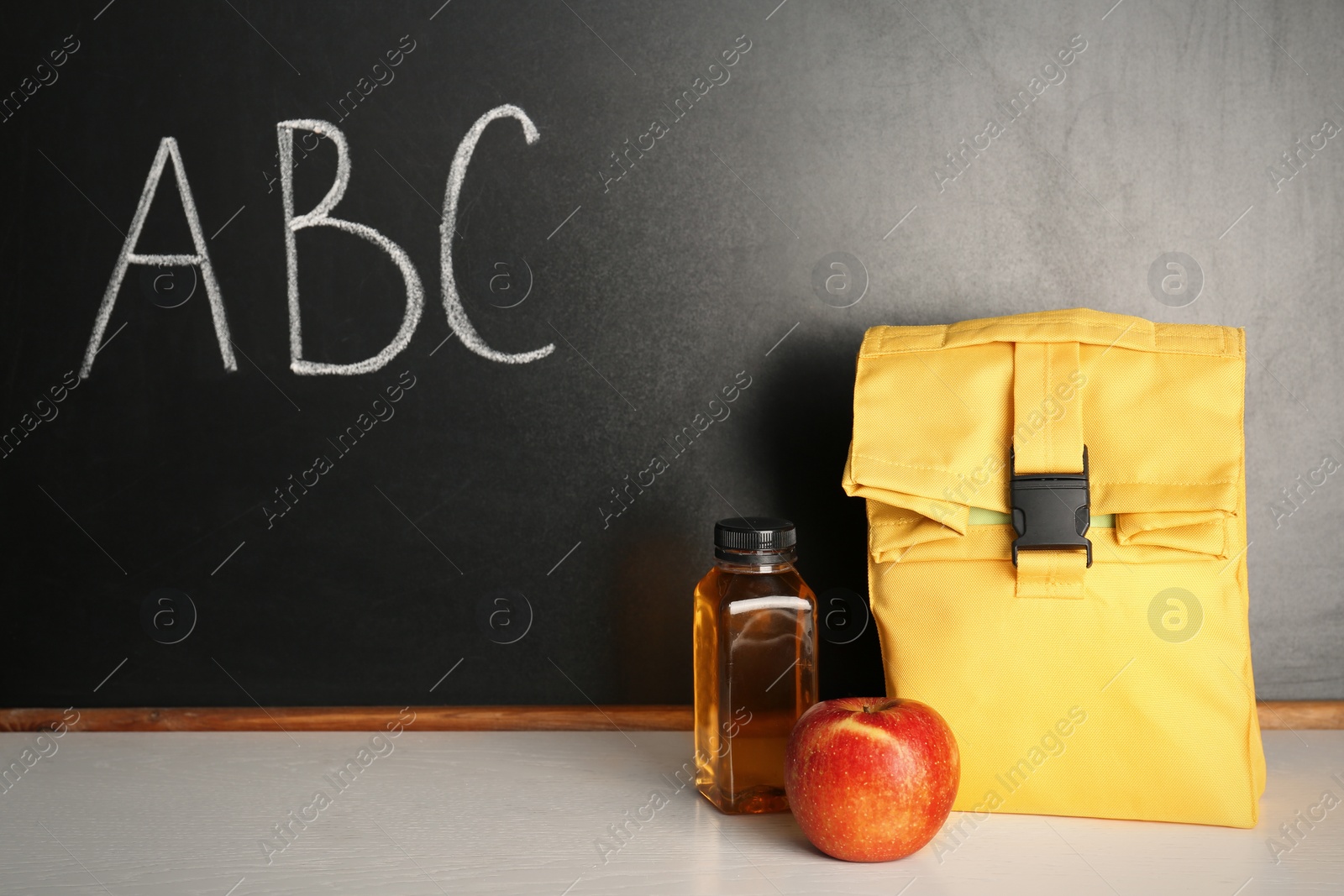 Photo of Healthy food for school child in lunch bag on table near blackboard with chalk written letters