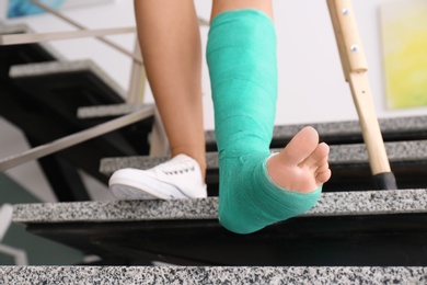 Photo of Young woman with crutch and broken leg in cast on stairs