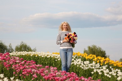 Happy woman with spring bouquet of flowers in beautiful tulip field on sunny day