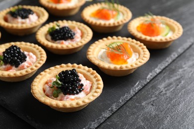 Photo of Delicious canapes with salmon and caviar on black textured table, closeup