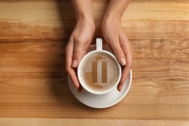 Image of Coffee Break. Woman holding cup of americano with milk at wooden table, top view