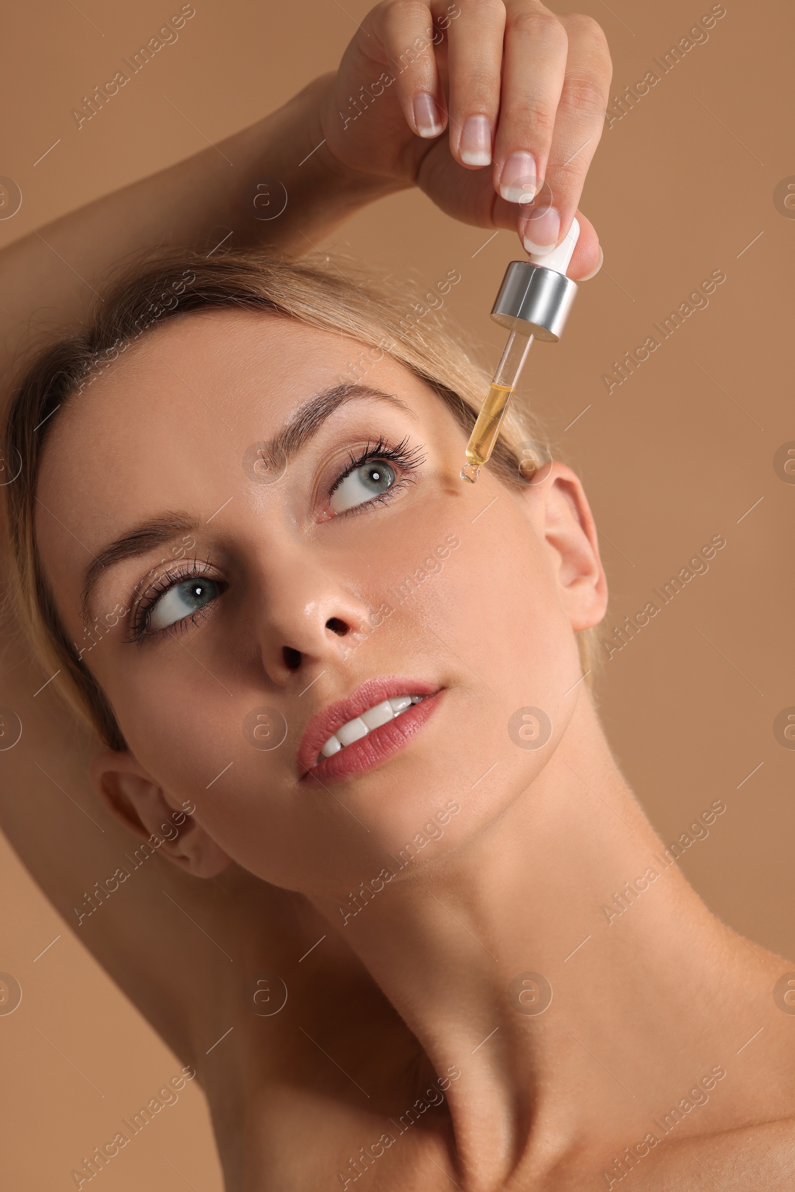 Photo of Beautiful woman applying cosmetic serum onto her face on beige background