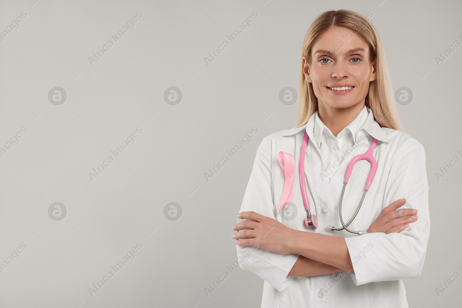 Photo of Doctor with pink ribbon and stethoscope on light grey background, space for text. Breast cancer awareness