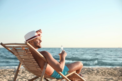 Young man relaxing in deck chair on beach near sea