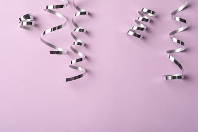 Shiny silver serpentine streamers on pink background, flat lay. Space for text