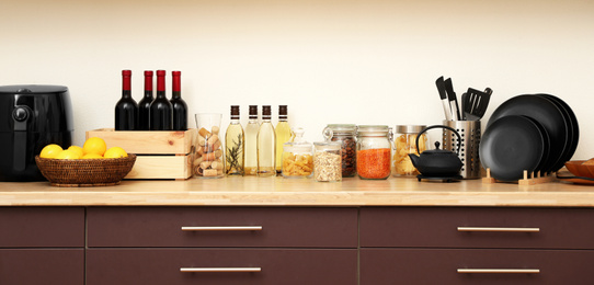 Wooden countertop with dishware and products near white wall. Kitchen interior idea