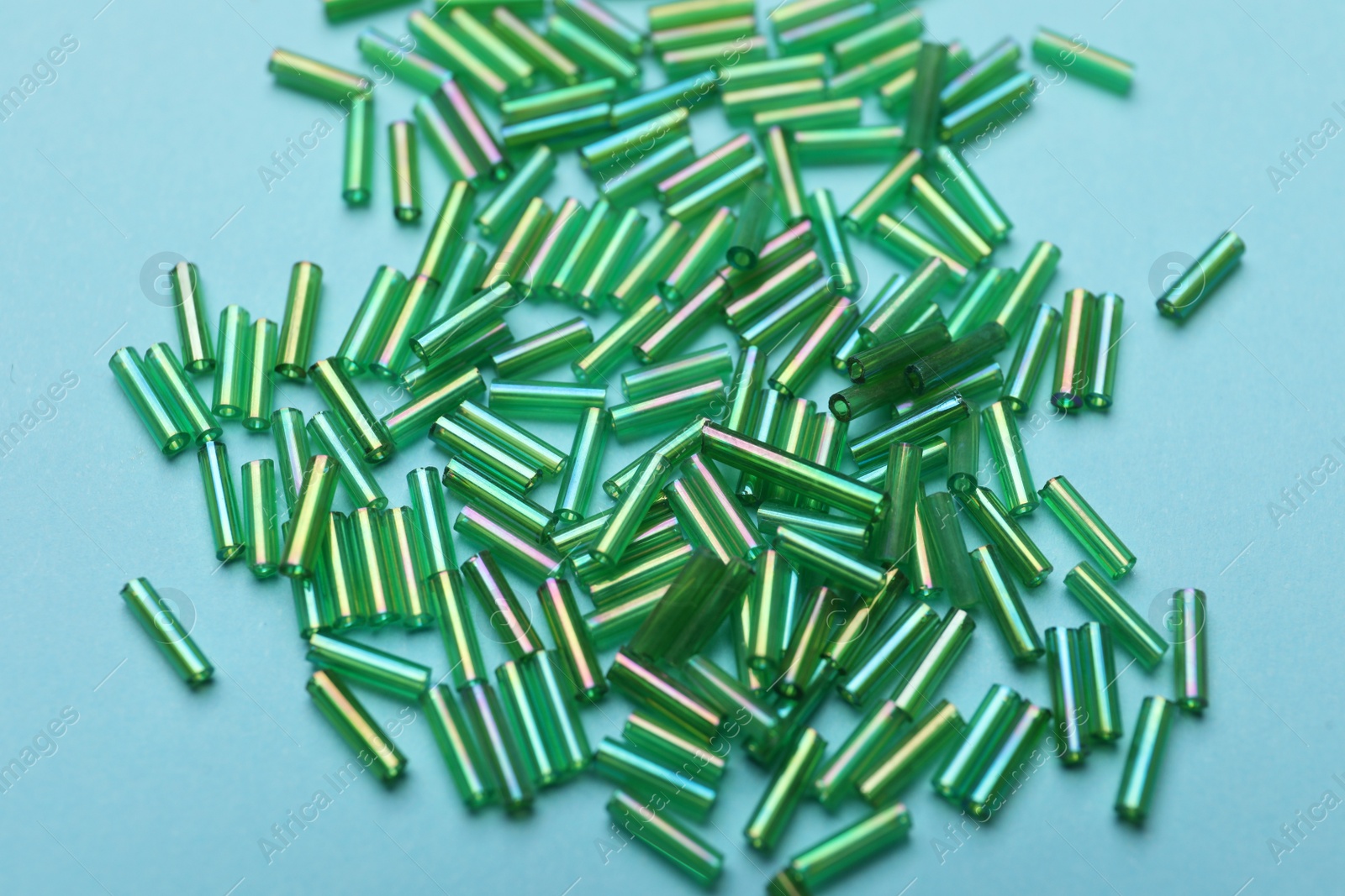 Photo of Pile of green bugle beads on light blue background, closeup