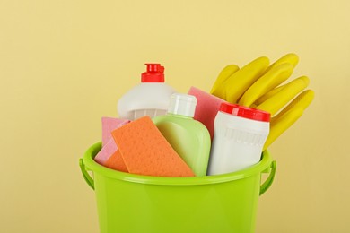 Photo of Bucket with different cleaning supplies against beige background, closeup