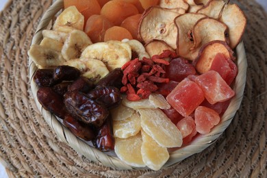 Photo of Wicker basket with different dried fruit on mat, top view