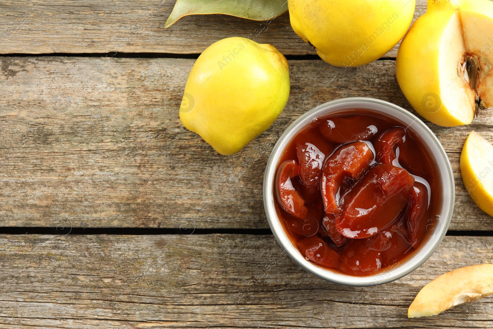 Photo of Tasty homemade quince jam in bowl and fruits on wooden table, flat lay. Space for text