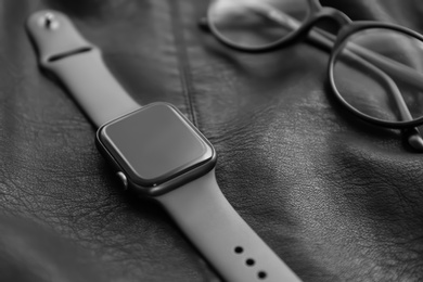 Photo of Stylish smart watch and glasses on black leather fabric, closeup
