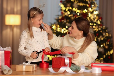 Christmas presents wrapping. Mother and her little daughter decorating gift box with ribbon at home