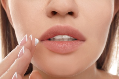 Image of Young woman with cold sore applying cream on lips, closeup