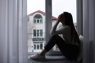 Photo of Unhappy young woman crying near window indoors, space for text. Loneliness concept
