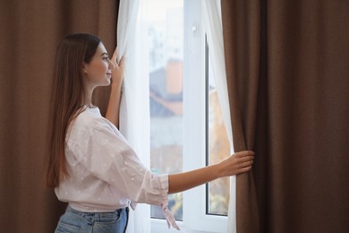 Photo of Woman opening elegant window curtains in room