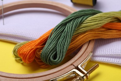 Embroidery hoop and threads on yellow background, closeup