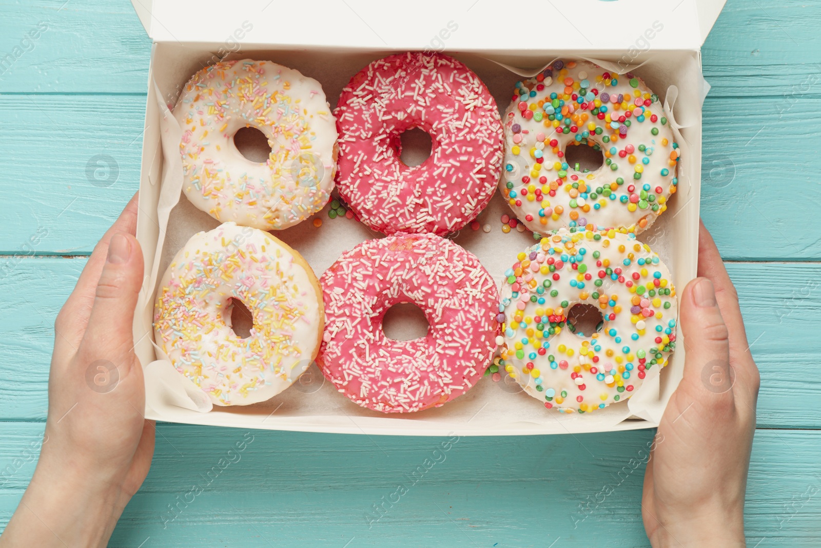 Photo of Woman with box of delicious glazed donuts at blue wooden table, top view