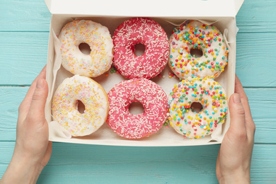 Photo of Woman with box of delicious glazed donuts at blue wooden table, top view
