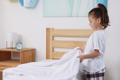 Cute girl changing bed linens in children room