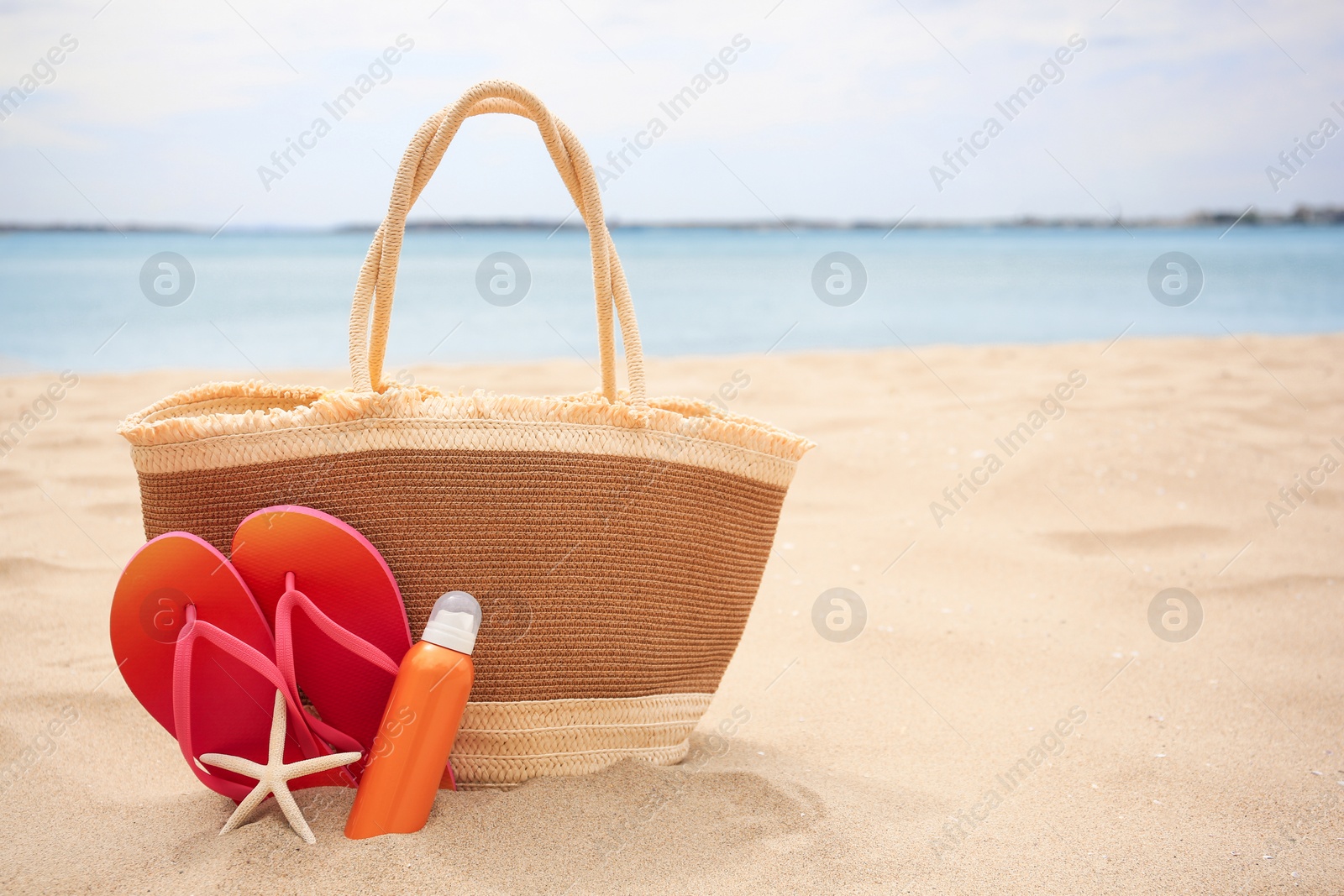 Photo of Straw bag, flip flops, starfish and sunscreen on beach, space for text