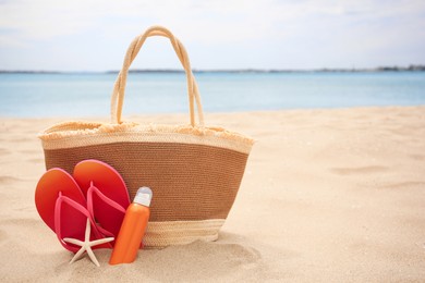 Photo of Straw bag, flip flops, starfish and sunscreen on beach, space for text